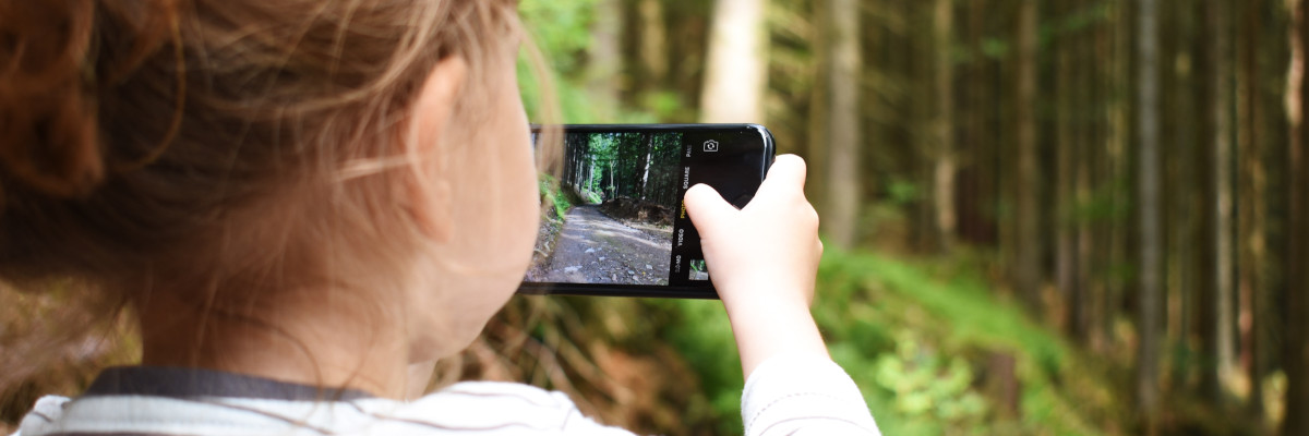 Per i genitori, consentire l'uso del cellulare da parte dei figli piccoli è un problema Bambina che con il cellulare inquadra un bosco per fare la foto