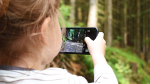 Bambina che con il cellulare inquadra un bosco per fare la foto