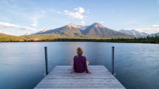 Donna su un molo lacustre, vista di spalle rivolta alle montagne. Spesso, il verbo stare è molto più produttivo di fare